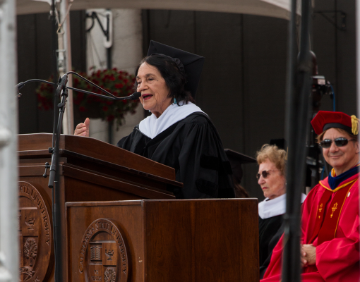 Delores Huerta stands at a lectern and speaks into a microphone.
