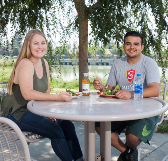 male and female student eating next to pond