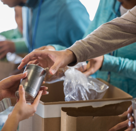 Person handing a can to someone else with people in the background preparing food boxes