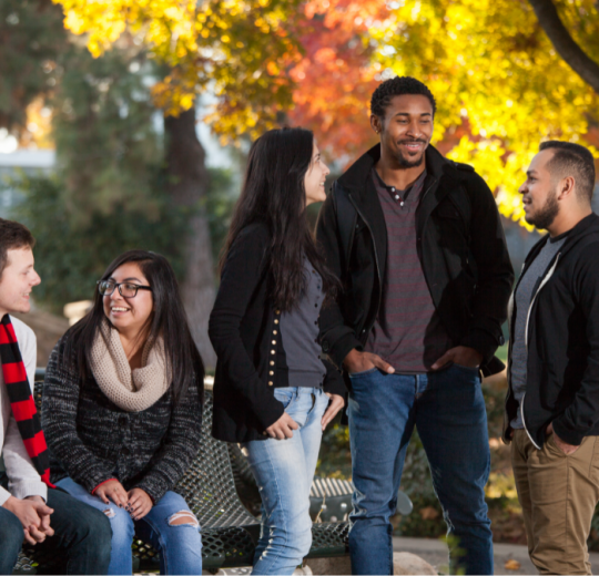 Five students pose for a group photo beside beautiful autumn trees.