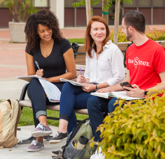 Three students talking to one another while sitting on a bench.