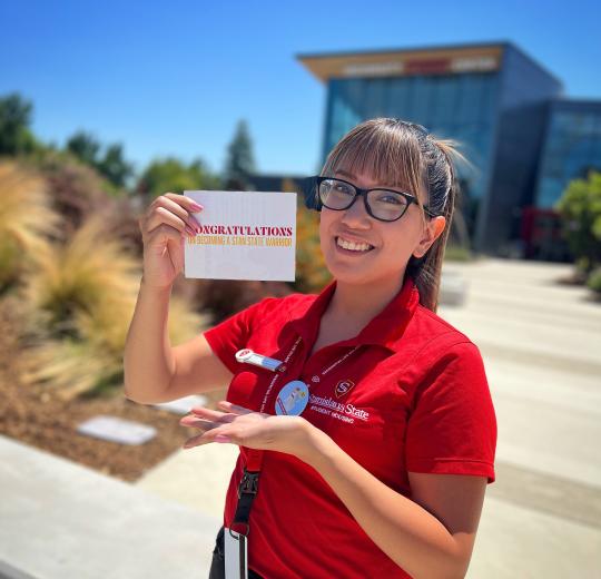 academic advisor holding a congrats on becoming a warrior card in front of the student center
