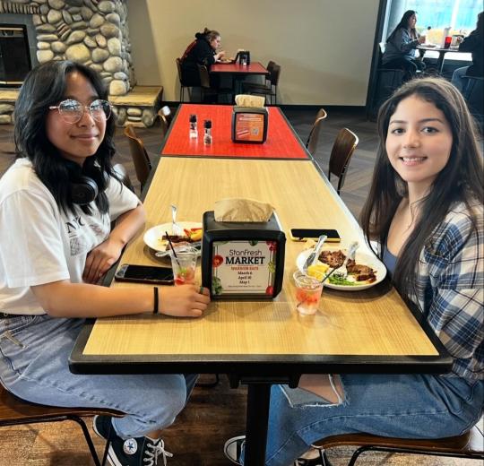 two female students sitting at a dining table eating