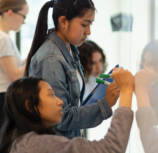 Students write on a whiteboard at the Learning Commons at Stan State