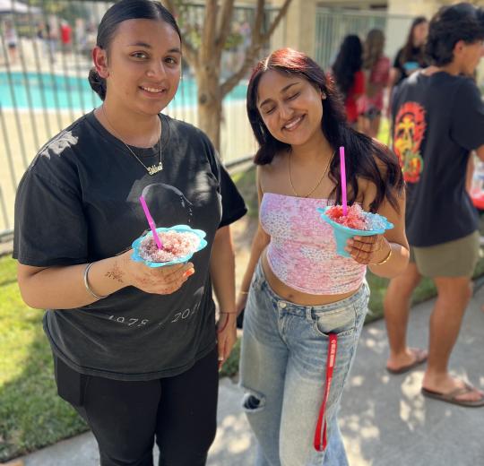 two female students smile at camera while holding snowcones at the welcome bbq