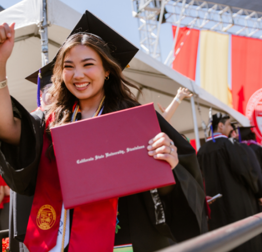 Stan State graduate smiling and holding her diploma cover during Commencement.