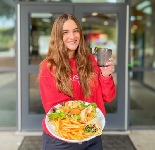 A student is in-focus holding a cuisine dish from Main Dining