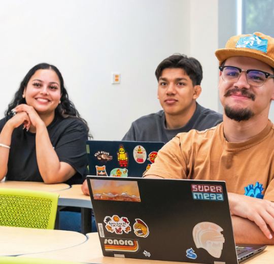 Three Stan State students seated in a classroom with laptops.