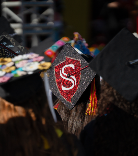 Graduating student with the Stan State shield on their mortar board.