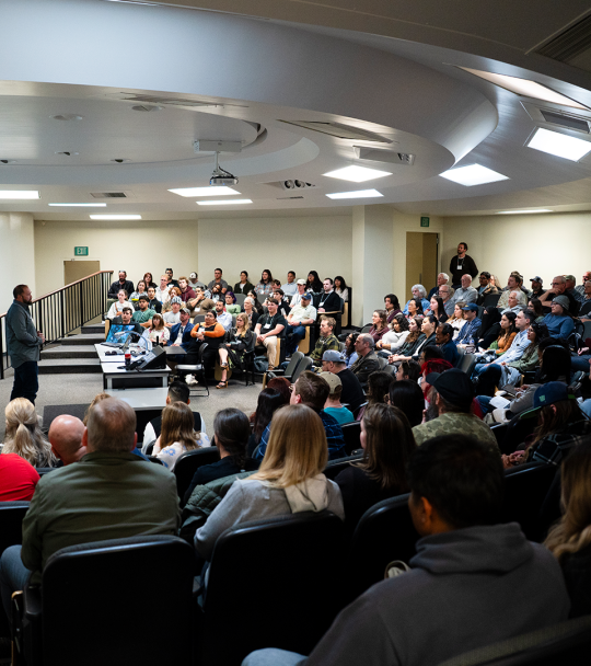 People seated in a large classroom listening to a speaker.