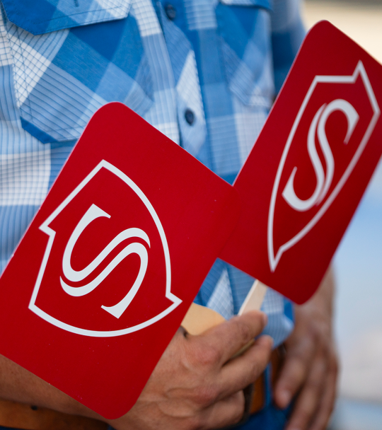 Hands holding fans decorated with the Stan State shield logo.