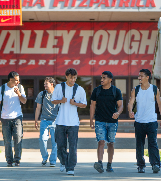 Five Stanislaus State students walk together on campus in front of the Fitzpatrick Arena.