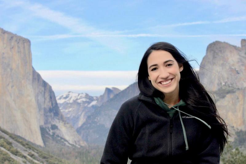 Victoria Martinez stands in front of a view of mountains and a blue sky at Yosemite National Park.